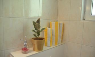 A bright bathroom corner with a potted plant and yellow-white towels. Next to the plant is a soap dispenser on a white shelf.
