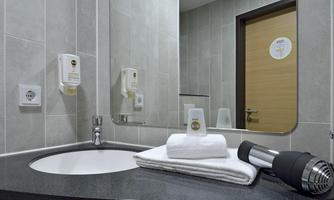 A modern bathroom with a sink, towels, and a hairdryer. The walls are in neutral gray tones.