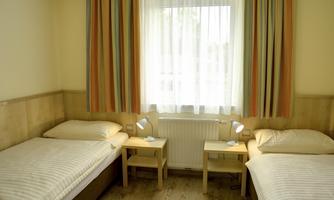 A simple room with two single beds and two nightstands. Bright curtains hang in front of the window, allowing natural light to come in.