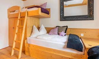 A cozy room with a wooden loft bed and a small ladder. There are pillows and a warm blanket on the bed.