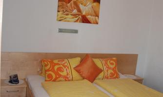 A cozy bedroom with a double bed and orange pillows. A picture hangs on the wall and the lighting creates an inviting atmosphere.