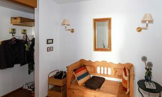 A cozy entrance area with a wooden bench and colorful cushions. Lamps hang on the wall and there is space for jackets and shoes.