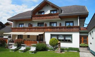 A beautiful house with a large balcony and a well-maintained garden. In the foreground, deck chairs are arranged on the lawn.