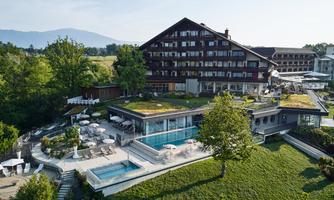 A modern hotel building with a beautiful garden and a pool. The surroundings are green and invite relaxation.