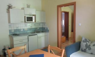 A bright kitchen with modern appliances and a dining area. In the background, a living room with a couch is visible.