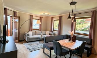 A modern living room with a dining area and a cozy sofa. Large windows let in plenty of daylight.