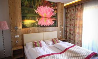 A cozy bedroom with a double bed and pretty bedding.  
On the wall hangs a large picture of a water lily, and the windows are adorned with floral curtains.