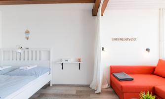 A modern room with a white bed and a red couch. The walls are bright and the light is friendly.