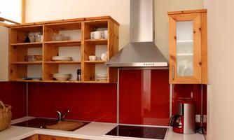 A modern kitchen with red walls and wooden shelves. The cooking area and appliances are well organized and functional.