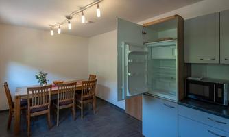 A modern kitchen with an open refrigerator and a dining table. The room is bright and welcoming with wooden chairs.