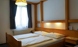A cozy bedroom with two single beds and wood paneling.  
Windows with curtains let in natural light.