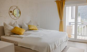 A modern bedroom with a large double bed and colorful cushions. Bright curtains and a mirror create a friendly atmosphere.