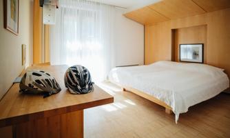 A bright room with a large bed and a desk. Two bicycle helmets are lying on the table.