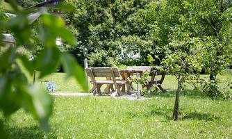 A tranquil garden with a green lawn and wooden furniture. In the background, numerous trees can be seen.