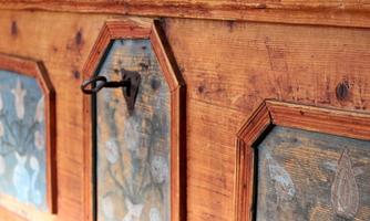 An antique wooden box with colorful, blooming motifs and a key. The wood surface is rustic and shows visible grain.