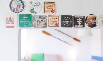 An arrangement of beer coasters on a wall. In the background, a few cushions and oars are visible.