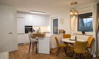 A modern kitchen with a dining area. The furniture is bright and stylish, and the floor is made of wood.