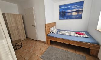 A simple room with a single bed, a desk, and a wardrobe.  
On the wall hangs a picture of a landscape with water and sky.