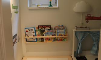 A cozy play area with a table and two chairs. On the wall are books and a scaled-down kitchen setup.