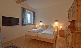 A cozy bedroom with a double bed, a television, and a wooden wardrobe. Bright walls and a warm ambiance give the room a relaxed atmosphere.