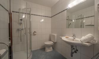 A modern bathroom with a shower, sink, and toilet. The walls are tiled, and there is comfortable lighting.