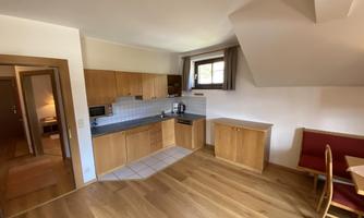 A modern kitchen with wooden cabinets and a dining area. The room has plenty of daylight and a warm flooring.