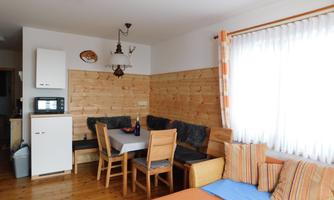 A cozy living area with wooden walls and a dining space. The large window front lets in plenty of light and creates an inviting atmosphere.
