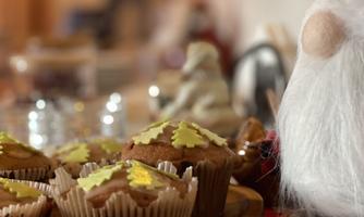 Delicious muffins with green sugar decoration are on a wooden tray. In the background, a Christmas figure can be seen.