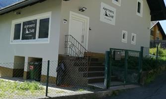 A modern house with a fenced garden and a staircase. In the foreground, there is a sign that says "Apartments."