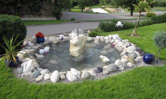 A small garden fountain with stones and plants.  
Surrounded by green meadows and a quiet path.