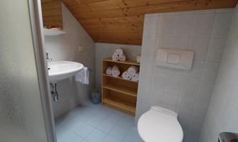 A small bathroom with a shower, a sink, and a toilet. Clean towels are neatly stacked.