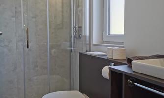 A modern bathroom with a shower and a toilet. The room is bright and has a wooden floor as well as a large window.