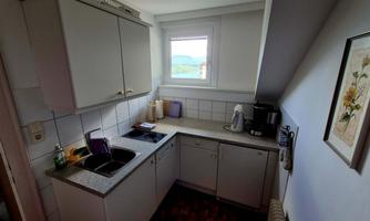 A bright kitchen unit with white cabinets and a window that opens up the view outside. The kitchen is modernly furnished and has a practical cooking area.