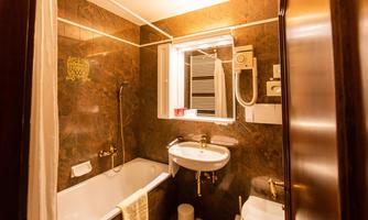 A modern bathroom with a bathtub, a sink, and a shower. The walls are clad in dark marble and a window provides daylight.