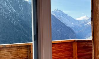 A balcony with a wooden railing and a view of impressive mountains. The clear sky and snow-capped peaks create an idyllic atmosphere.