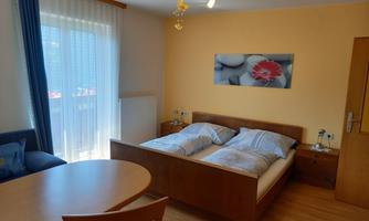 A cozy bedroom with a double bed and a round table. Large windows provide plenty of daylight.