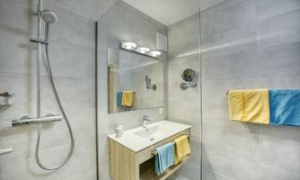 A modern bathroom with a glass shower and a simple sink. Towels in blue and yellow hang on the wall.
