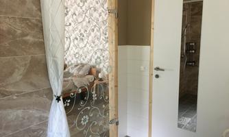 A modern bathroom with frosted glass and tiles in neutral colors. In the background, a bright room can be seen, which may be a bedroom.