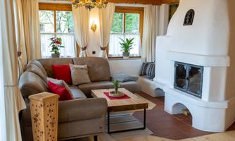 A cozy living room with a beige couch and red cushions. The fireplace and the windows provide an inviting atmosphere.