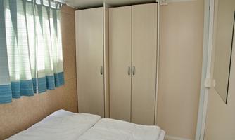A cozy sleeping area with a double bed and a fitted wardrobe. The windows are adorned with blue curtains that let in some daylight.