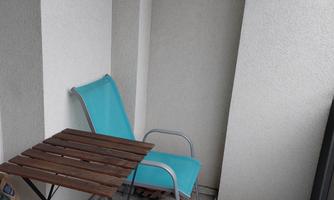A small balcony with a blue chair and a folding table. The walls are light and the tiles are gray.