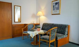 A cozy room with a sofa and two chairs. Next to a table is a lamp and a small pot with a plant.