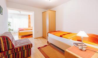A bright bedroom with two single beds and a cozy seating area. The room features warm colors and plenty of natural light.