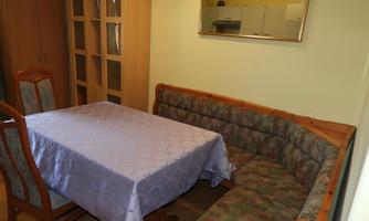 A cozy dining area with a table and a seating nook. The walls are light and there are shelves in the background.