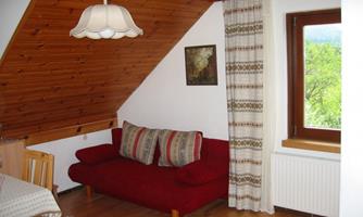A cozy room with a red couch and wooden walls. A table and windows overlooking nature complete the furnishings.