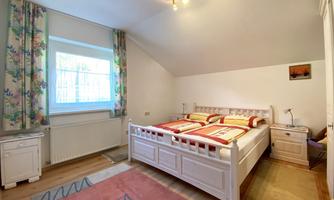 A bright bedroom with a large white bed and colorful curtains. The windows let in plenty of light and the floor is made of wood.
