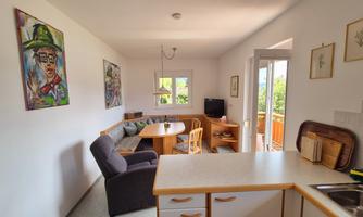 A bright and inviting apartment with a round dining table and cozy seating. Artistic pictures hang on the wall, and the window offers a view of the outdoors.
