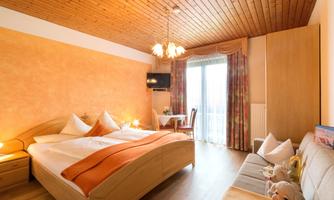A cozy bedroom with a double bed and wooden walls. The room has large windows and a pleasant atmosphere.