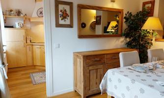 A cozy dining area with a wooden table and a wooden sideboard. In the background, the kitchen with modern appliances can be seen.
