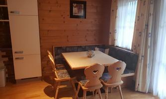 A cozy dining area with wooden paneling and a large table group. The room has large windows that let in plenty of daylight.